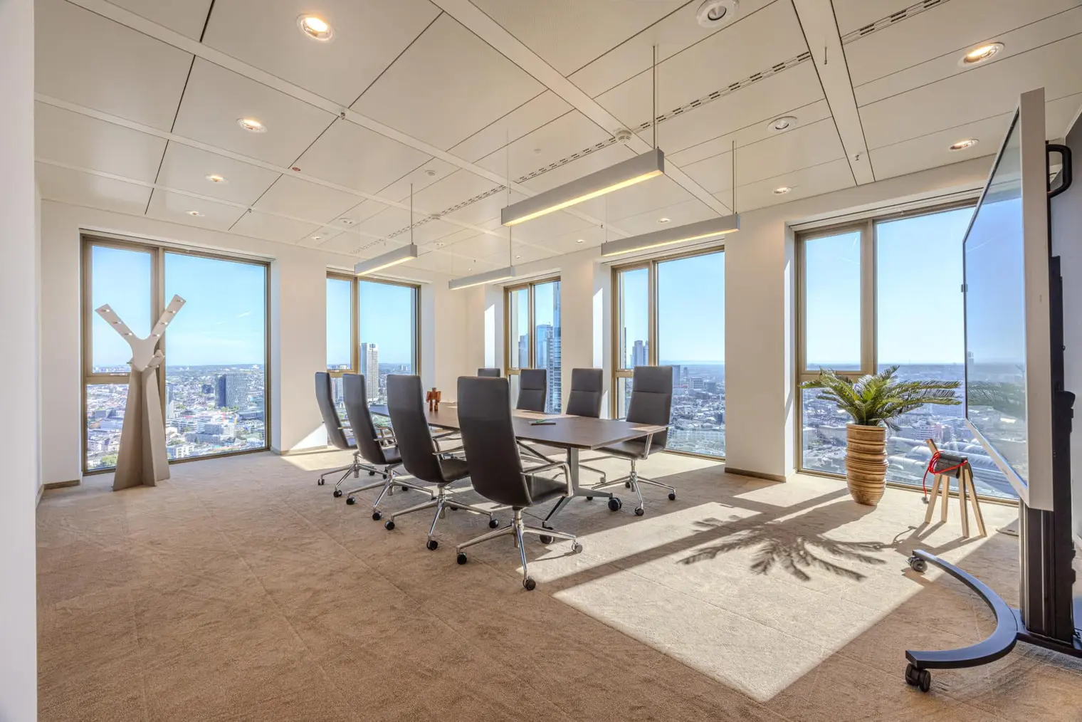 Besprechungsraum „City West“ mit Konferenztisch, mobilem Display und Fensterfronten