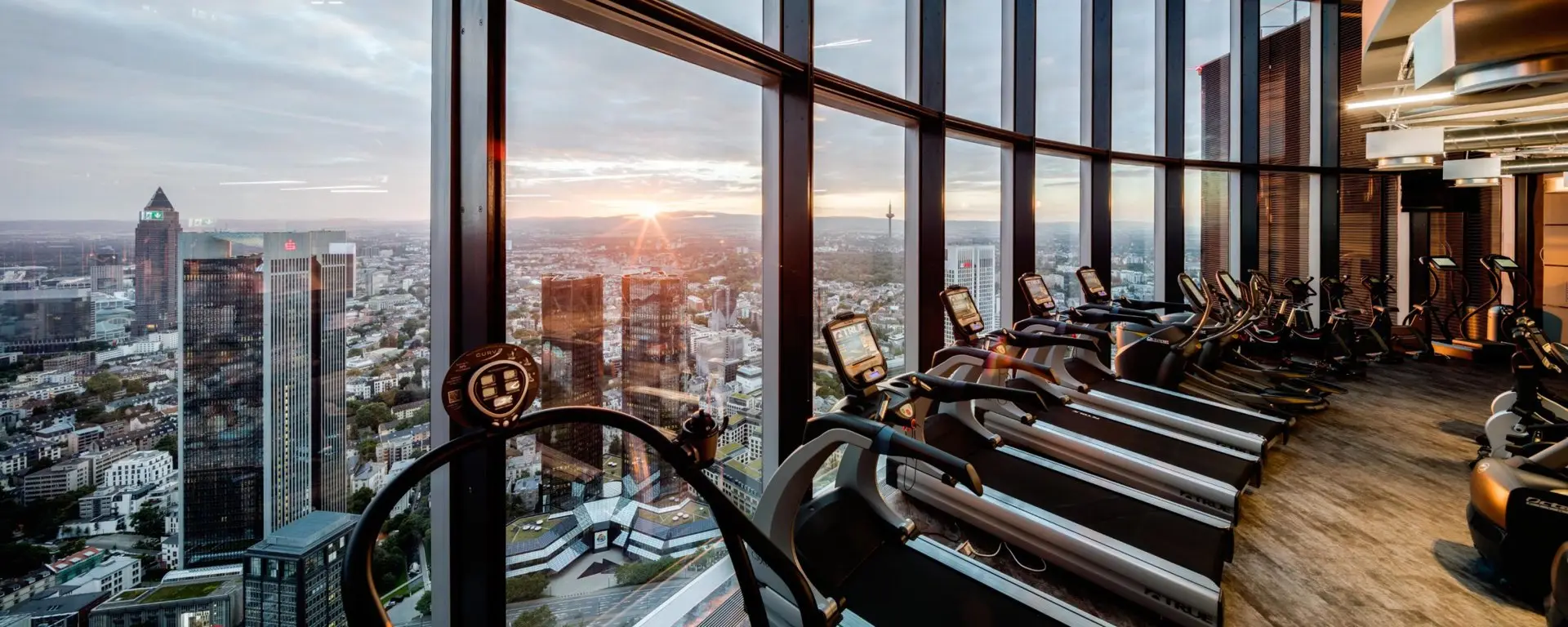 Treadmills in front of the glass facade of the gym at Main Tower with a view of the Frankfurt skyline