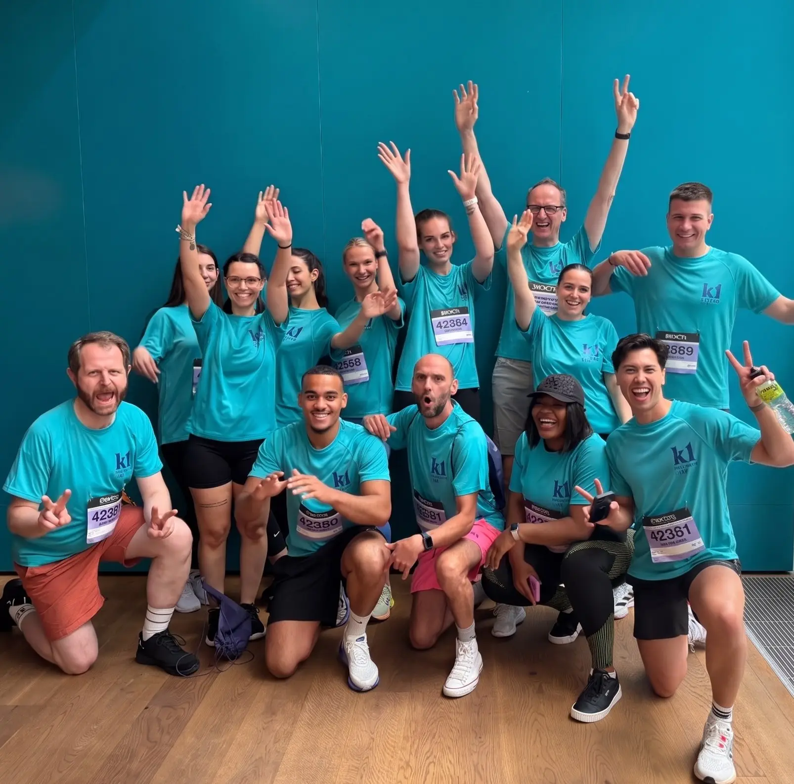 The k1 BusinessClub team in turquoise k1 running shirts with race numbers, cheering in front of a petrol-colored wall in Frankfurt